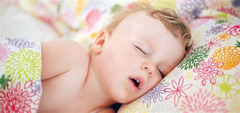 Kūdikis miega lovelėje, šalia ramiai sėdi mama ir stebi jį per monitorių