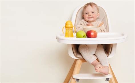 Kūdikis linksmai valgo maitinimo kėdutėje