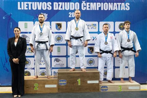 Juoda-balta nuotrauka, kurioje matyti dziudo kovotojai tatami ir teisėjas.